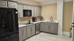 Una cucina con mobili grigi, un frigorifero nero, un forno a microonde, una macchina del caffè e un lavandino.