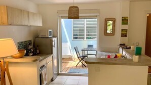 A compact kitchen with a dining area, a microwave, and a view through a glass door to an outdoor patio. - Kay Ti Sable - Appartement sur la plage (Le Diamant)