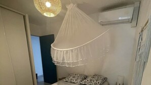 A bedroom with a bed, a hanging light fixture, an air conditioning unit, and a small table. - Kay Ti Sable - Appartement sur la plage (Le Diamant)