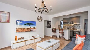 A modern living room with a sofa, a coffee table, and a TV mounted on the wall. There is a kitchen area visible in the background. - Sunset Escape Apartment Modern & Spacious Two Bedroom in Tatu City (Ruiru)