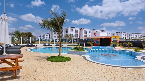 A pool area with lounge chairs, a palm tree, and a building with a colorful mural. - Sunset Escape Apartment Modern & Spacious Two Bedroom in Tatu City (Ruiru)