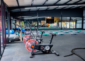 Ein Fitnessstudio mit Trainingsgeräten, einem großen Ventilator und einer Spiegelwand.