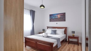 A neatly arranged hotel room with a wooden bed, a bedside table with a lamp, a painting on the wall, and a window with curtains. - Sunset Escape Apartment Modern & Spacious Two Bedroom in Tatu City (Ruiru)