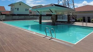 A swimming pool with a wooden deck, a water tower, and a building with a red-tiled roof. - Casa De Amor Villa 1338 - Panglao (Dauis)