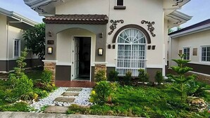 A two-story house with a central entrance, a large arched window, and a tiled roof. - Casa De Amor Villa 1338 - Panglao (Dauis)