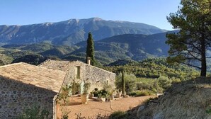 Un edificio de piedra con tejado de baldosas, rodeado de un jardín y un paisaje montañoso.