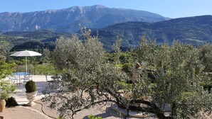 Un patio con mobiliario exterior, una sombrilla blanca y vistas a montañas.