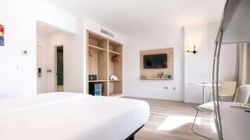 Una habitación de hotel moderna con una cama grande, armario empotrado, un televisor montado en la pared y una pequeña mesa con sillas.