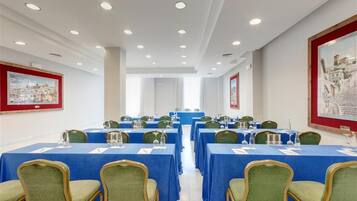 Un salón de conferencias con mesas dispuestas para reuniones, sillas verdes y cuadros en las paredes.