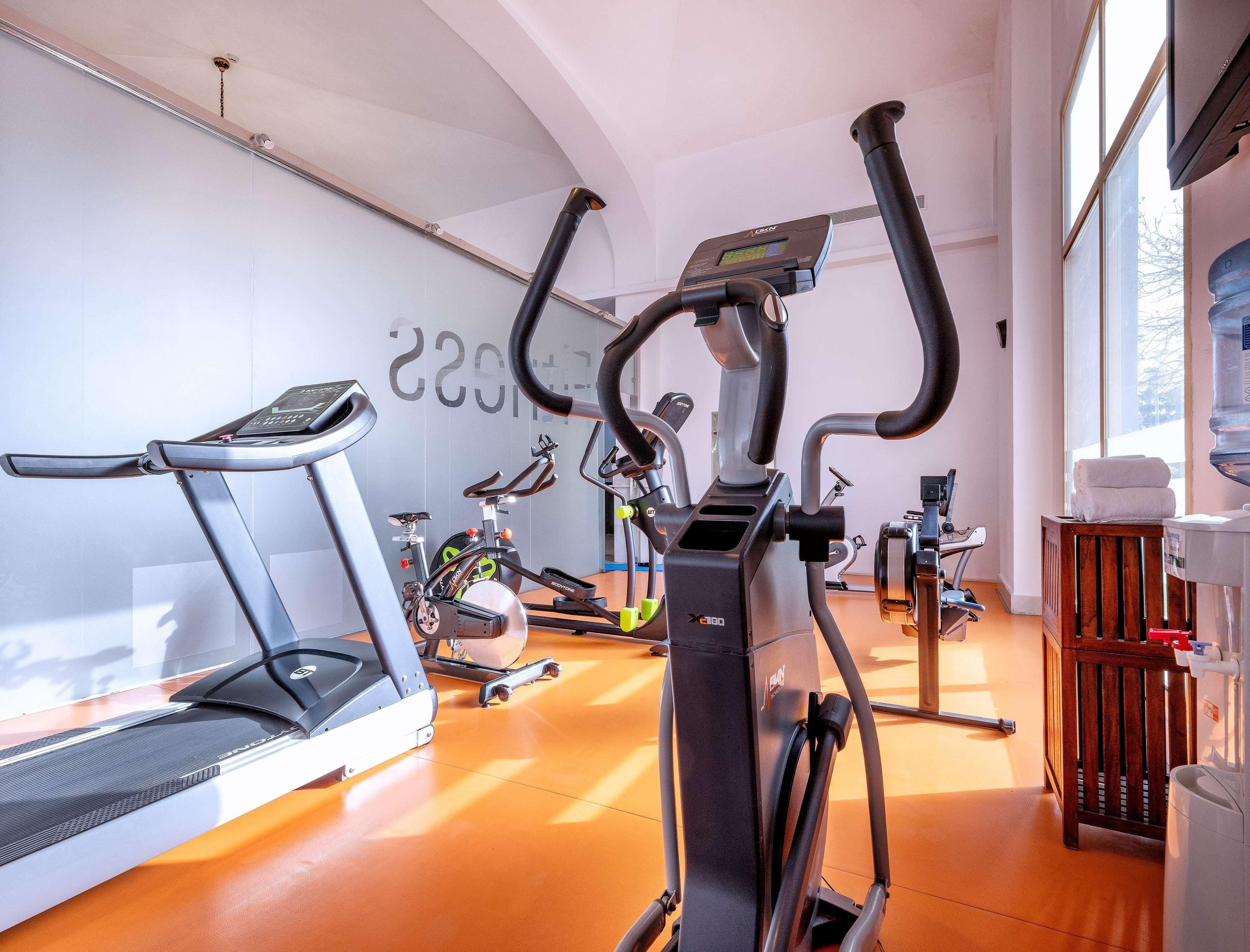 Un gimnasio con bicicletas estáticas, cinta de correr y dispensador de agua.