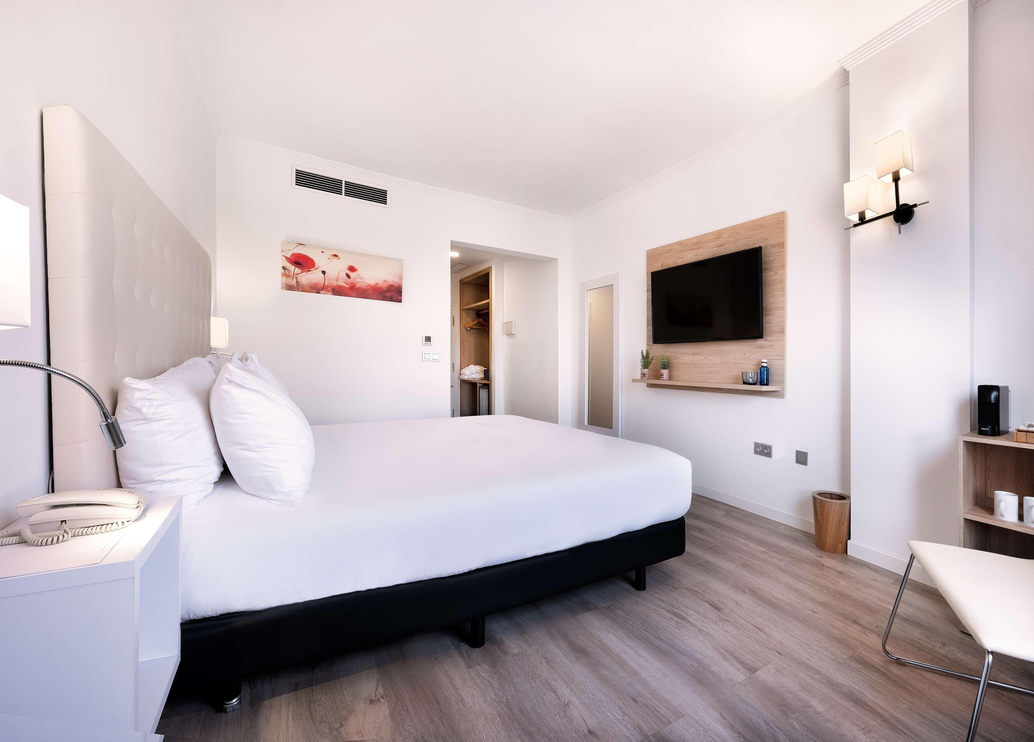Une chambre d’hôtel moderne avec un grand lit, une table de chevet, une lampe et un téléviseur fixé au mur.
