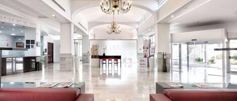A spacious lobby with a chandelier, a reception desk, and a seating area.