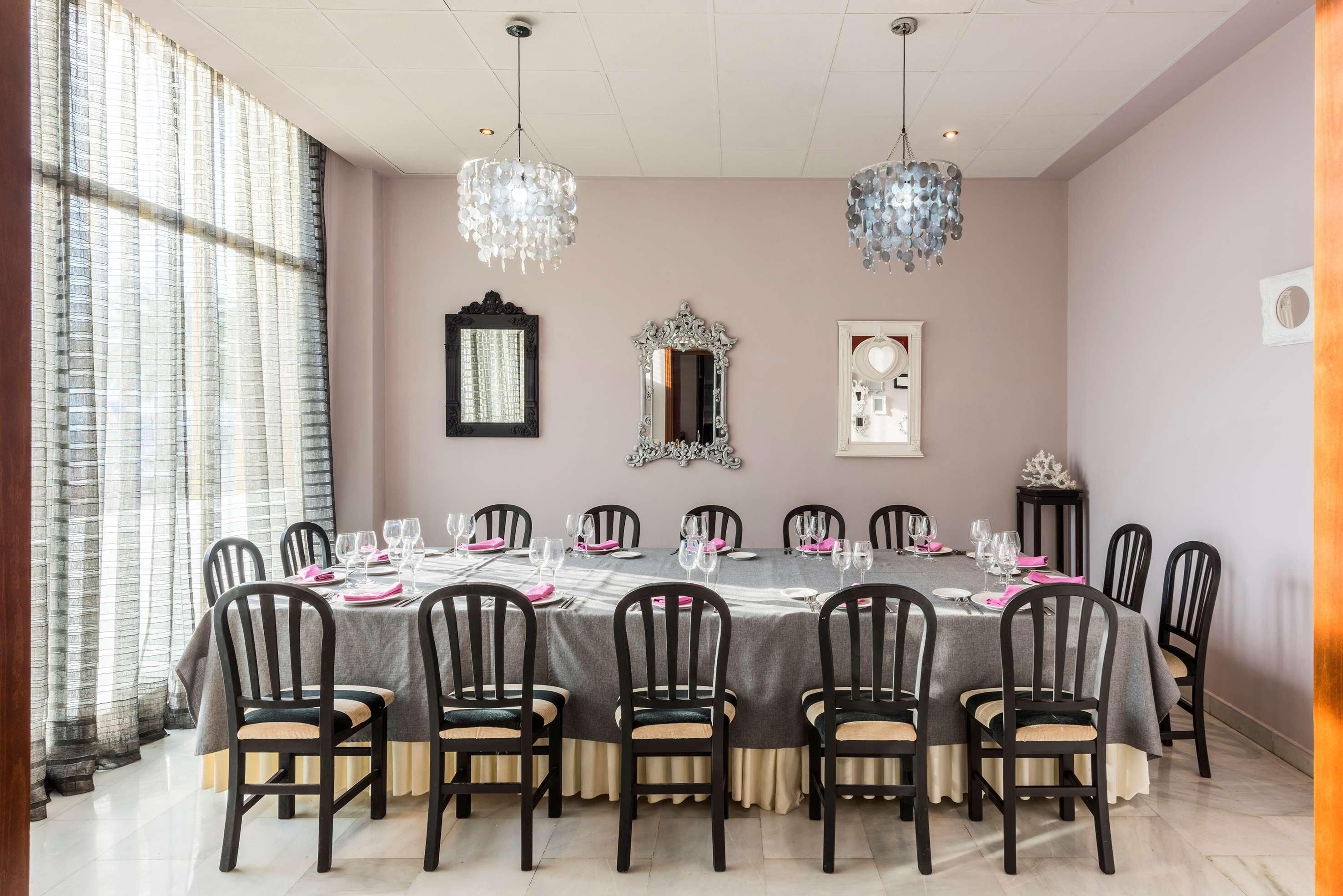 A dining room with a round table set for 12, surrounded by chairs, with chandeliers and wall mirrors.