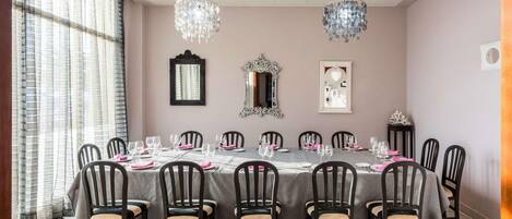 A dining room with a round table set for 12, surrounded by chairs, with chandeliers and wall mirrors.