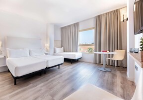 Habitación de hotel con dos camas, una mesita, una silla y vistas a la ciudad.