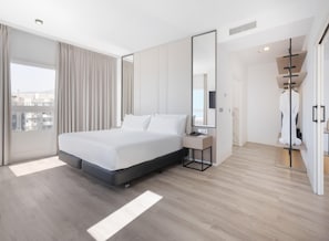 Quarto de hotel moderno com uma cama grande, uma mesa de cabeceira, um espelho e vista para a cidade.