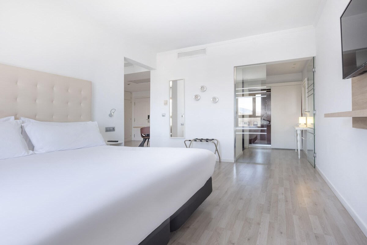 A modern hotel room with a large bed, a flat-screen TV, a bedside table, and a walk-in closet.