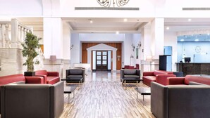 Eine geräumige Lobby mit einem prunkvollen Kronleuchter, roten und schwarzen Sitzgelegenheiten, einem Empfangstresen und einer Treppe.