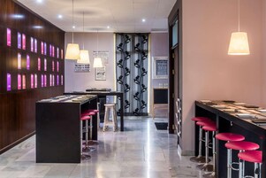 Un área de bar moderna con una barra alargada, taburetes rojos y luces colgantes.