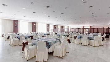 A large banquet hall with multiple round tables, each set with white chairs and tablecloths.