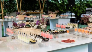 Ein Buffet mit verschiedenen Speisen und Getränken, ein Korbwesen und ein Lautsprecher in einem Garten.