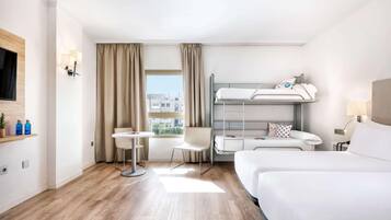 Habitació d'hotel amb un llit superposat, una taula, una cadira i una finestra amb cortines.