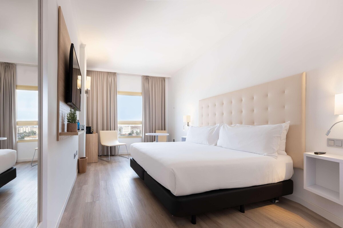 Una camera d'albergo con un letto grande, una TV a muro, un tavolino e una sedia.
