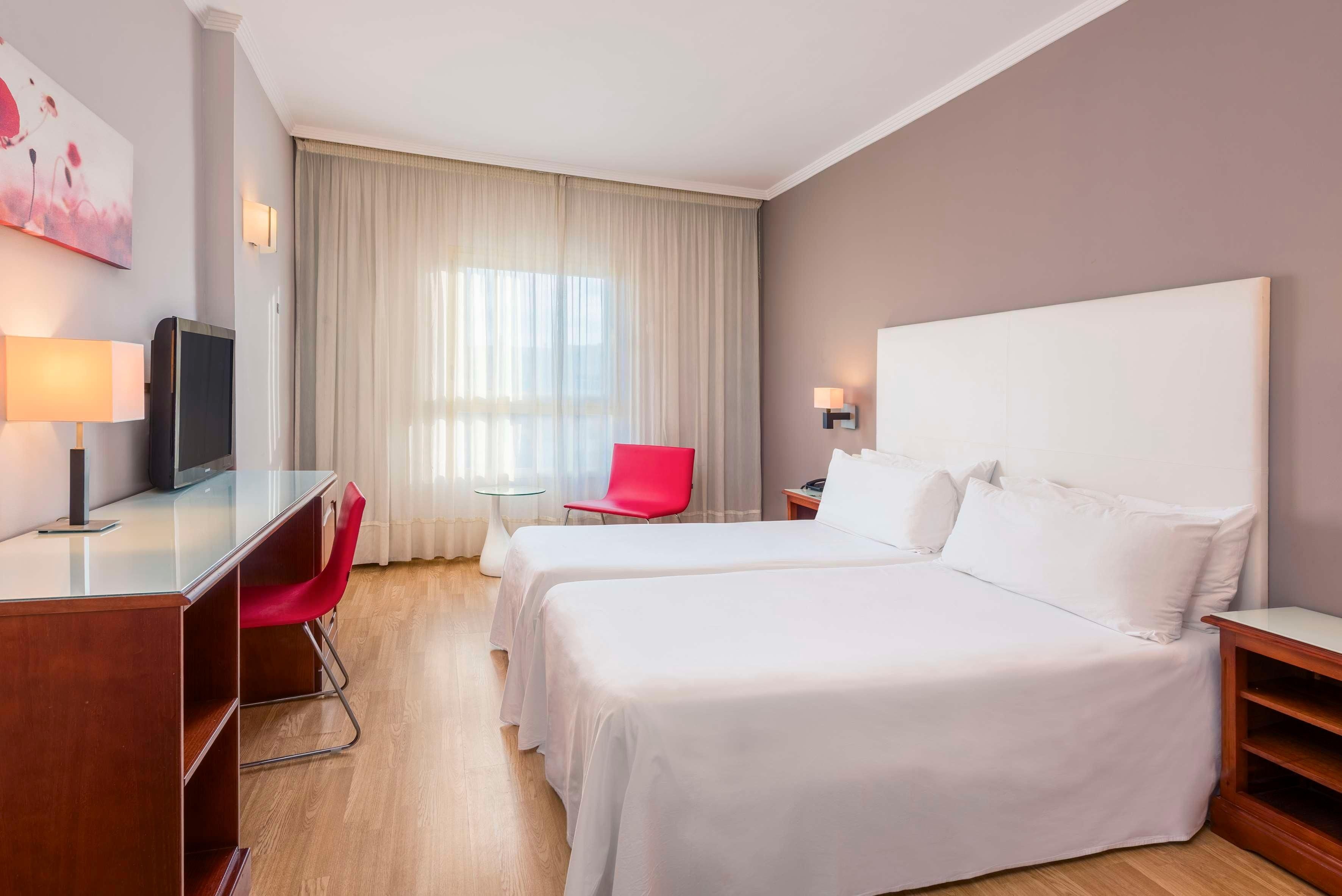 A hotel room with a bed, desk, chair, TV, and a window with curtains.
