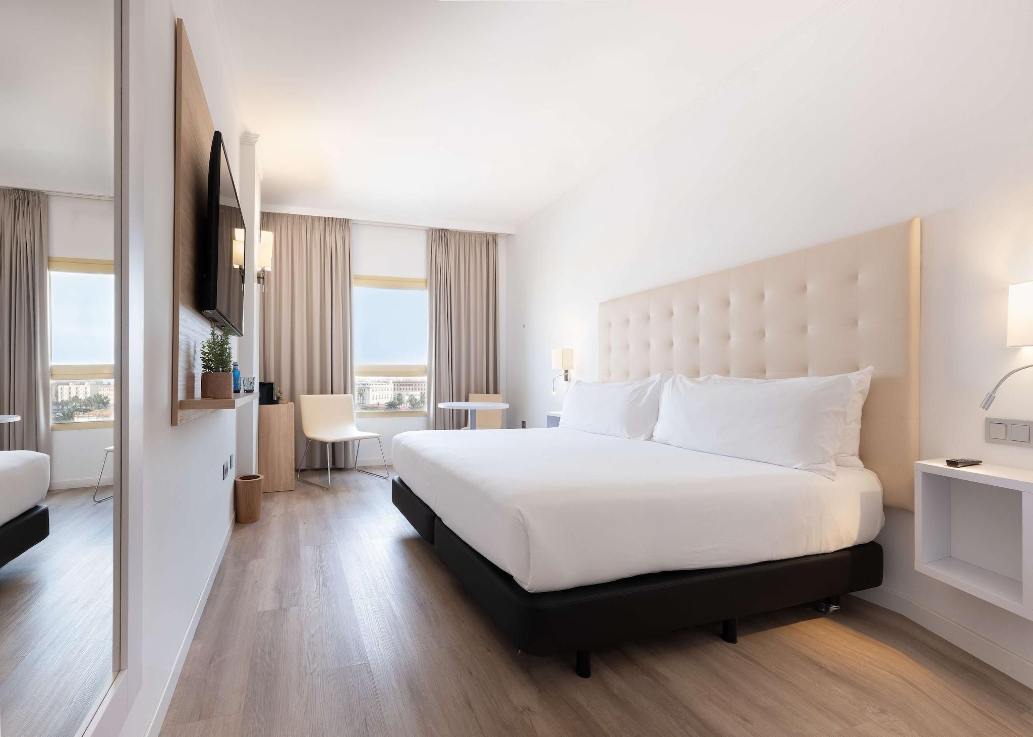 A hotel room with a large bed, a TV mounted on the wall, a small table, and a chair.