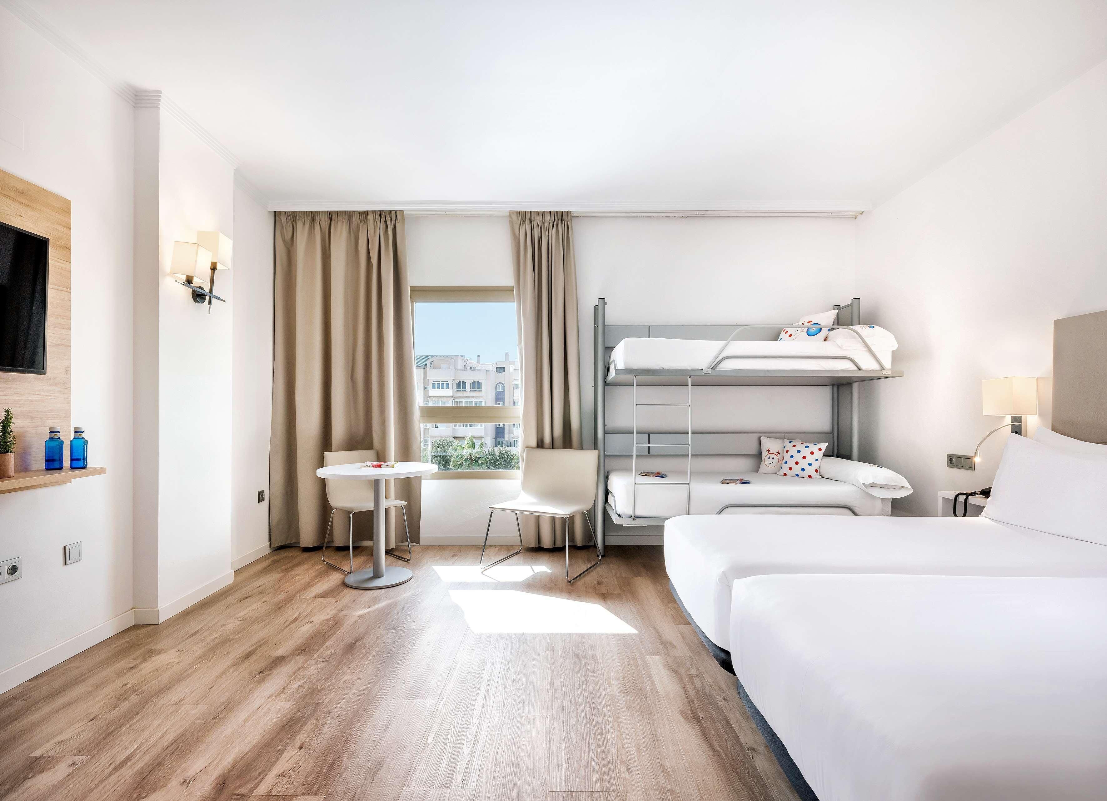 Une chambre d’hôtel avec un lit superposé, un bureau, une chaise, une petite table et un téléviseur.