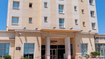 Un hotel de varios pisos llamado 'MELILLA PUERTO' con una entrada central, un restaurante visible llamado 'Galecon Restaurante' y un cielo azul despejado al fondo.