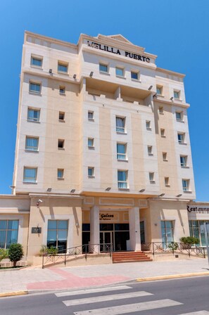 A multi-story hotel named 'MELILLA PUERTO' with a central entrance, a visible restaurant named 'Galecon Restaurante,' and a clear blue sky in the background. - Melilla Puerto Hotel (Melilla)