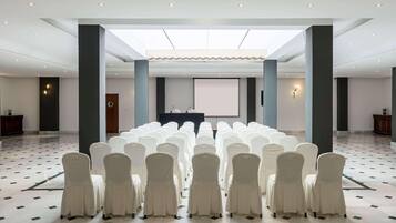Une salle de conférence avec des rangées de chaises blanches, un pupitre et un écran de projection.