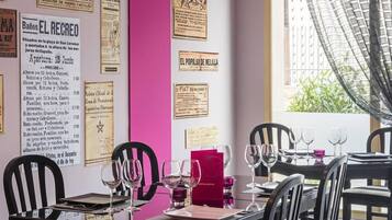 Interior de un restaurante con una pared de acento rosa, varios menús a la vista y una zona de comedor con mesas dispuestas para los clientes.