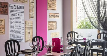 Interior de un restaurante con una pared de acento rosa, varios menús a la vista y una zona de comedor con mesas dispuestas para los clientes.