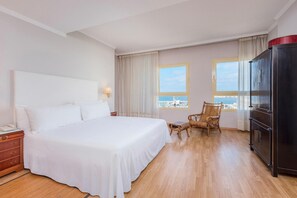 A hotel room with a large bed, a television, a wardrobe, a desk with a lamp, and a view of the sea. - Melilla Puerto Hotel (Melilla)