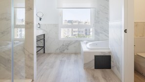 Ein modernes Badezimmer mit einer Badewanne, einer Dusche und einem Fenster mit Blick auf Gebäude.