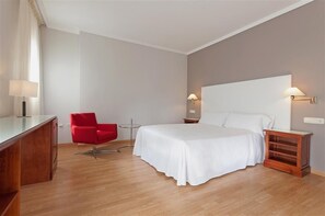 Habitación de hotel con cama, una silla roja, escritorio y dos lámparas fijadas a la pared.