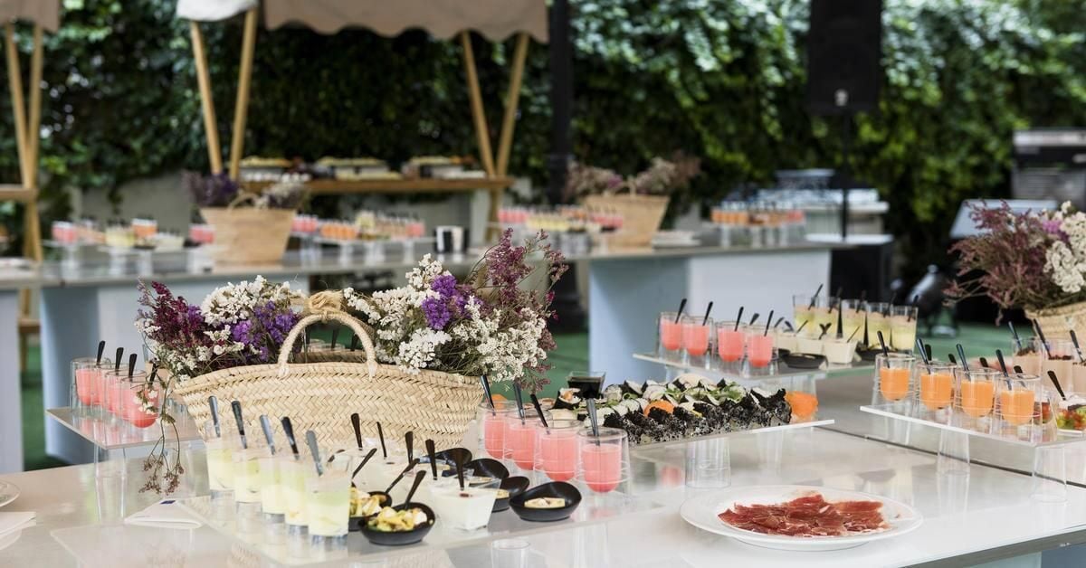 Montaje de bufé con diversas opciones de comida y bebidas, incluyendo una cesta de flores y un plato de fiambres.