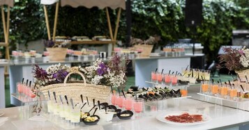 Montaje de bufé con diversas opciones de comida y bebidas, incluyendo una cesta de flores y un plato de fiambres.