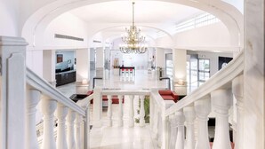 Eine geräumige Hotelhalle mit einer imposanten Treppe, einer Kristallleuchtre und einem Empfangstisch.