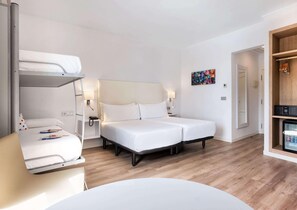 Quarto de hotel moderno com beliche, uma cama de solteiro, mesas de cabeceira com luminárias, um refrigerador e um quadro colorido na parede.