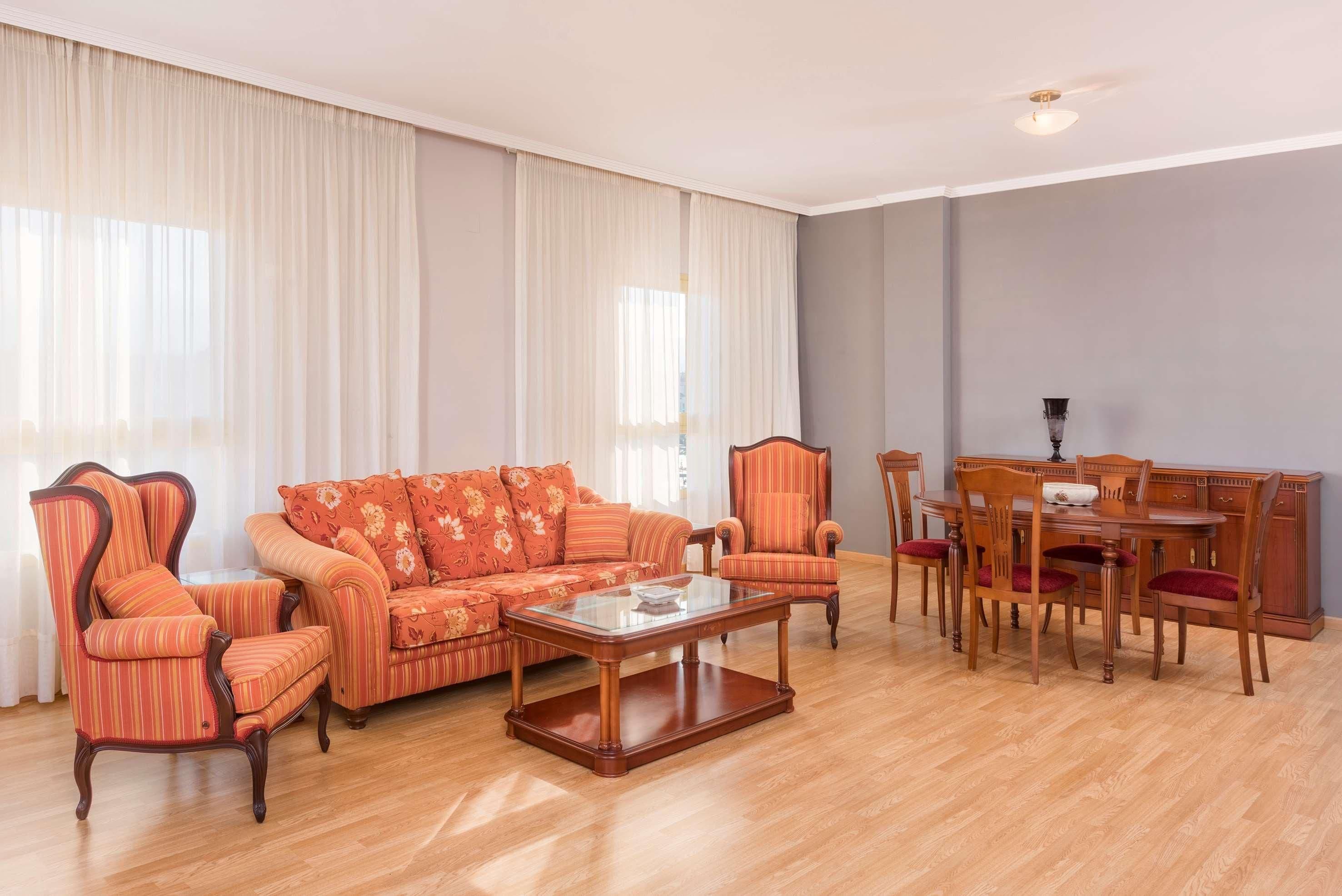 Una sala de estar con un sofá, sillones, una mesa de centro, una mesa de comedor con sillas y una araña.
