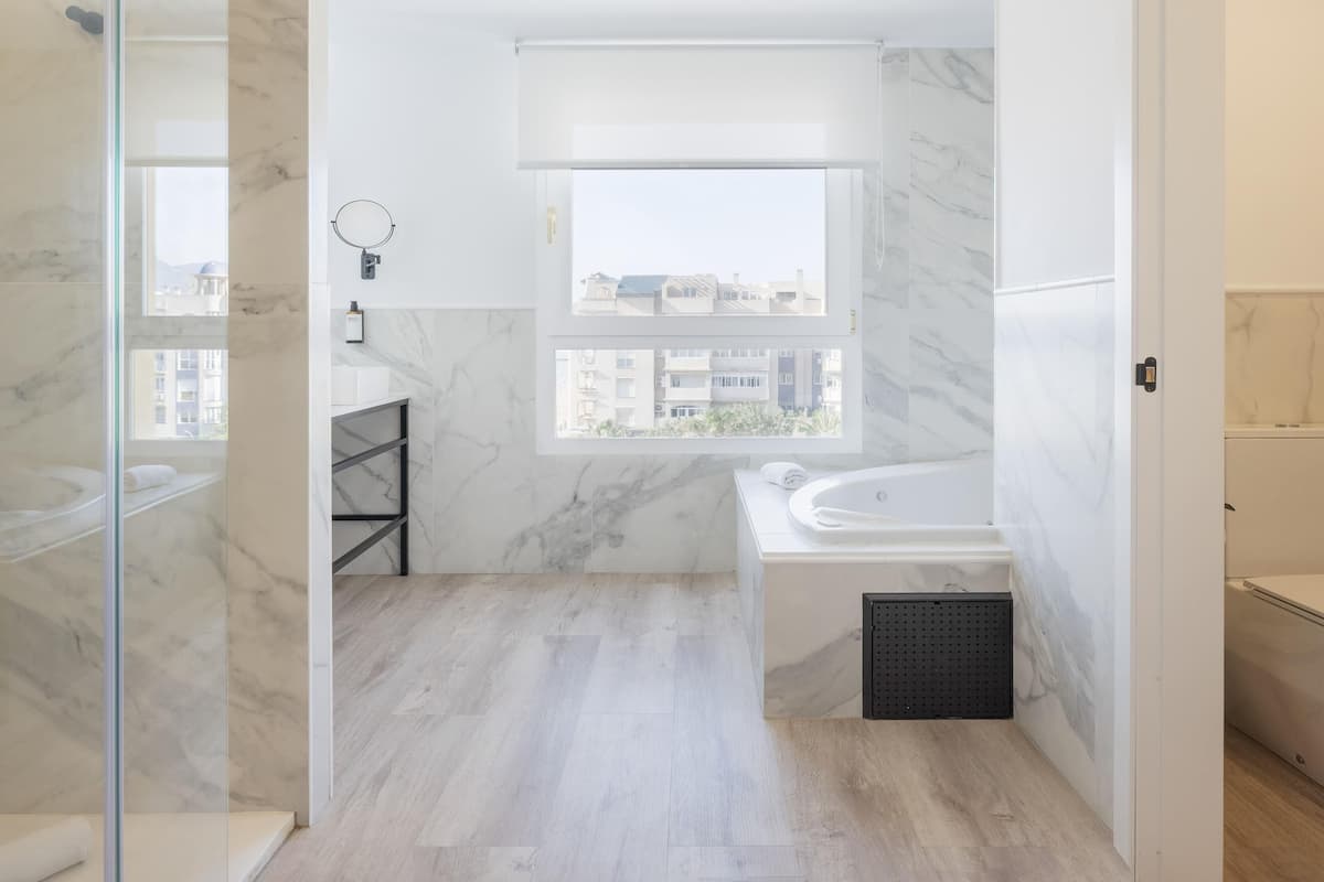 A modern bathroom with a bathtub, a shower, and a window with a view of buildings.