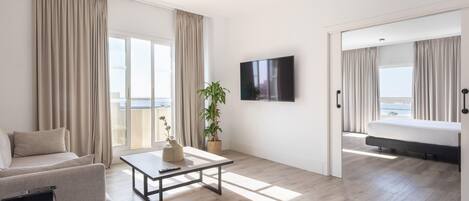 A modern hotel room with a sofa, a coffee table, a TV, a bed, and a balcony with curtains.