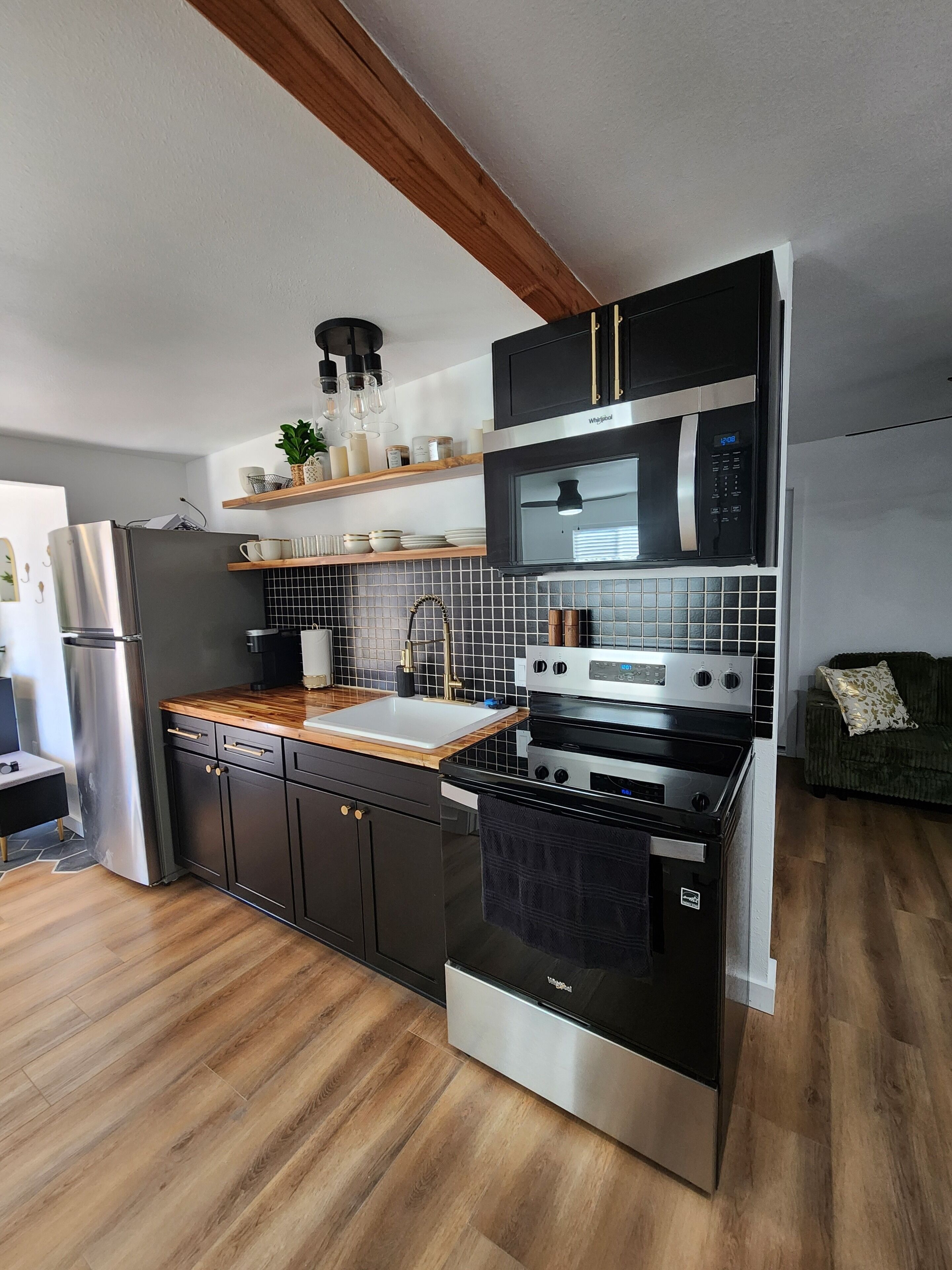 A modern kitchen with a stainless steel refrigerator, black and white microwave, double oven, and wooden countertops.