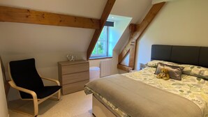 Ein Schlafzimmer mit einem großen Bett, einem Sessel, einer Kommode und einem Fenster.