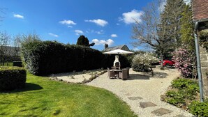 Ein Garten mit Grillplatz, einem Kiesweg und einem in der Nähe stehenden roten Auto.