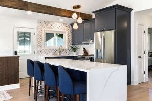 Une cuisine moderne avec un îlot en marbre, des meubles de couleur sombre et des tabourets de bar.