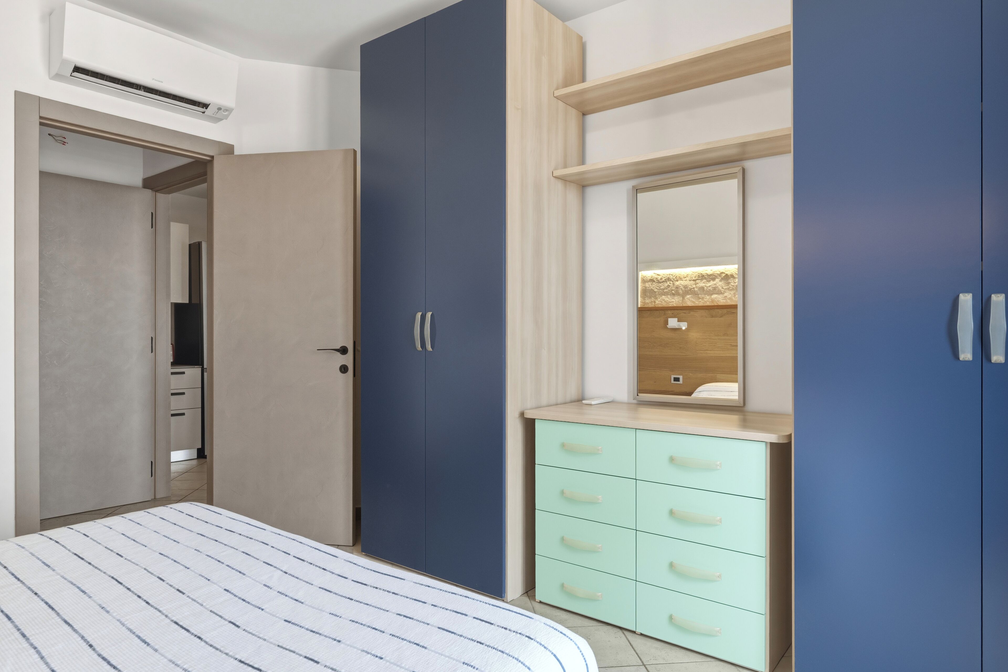 Een slaapkamer met een bed, een kledingkast, een kaptafel met lades en een spiegel.